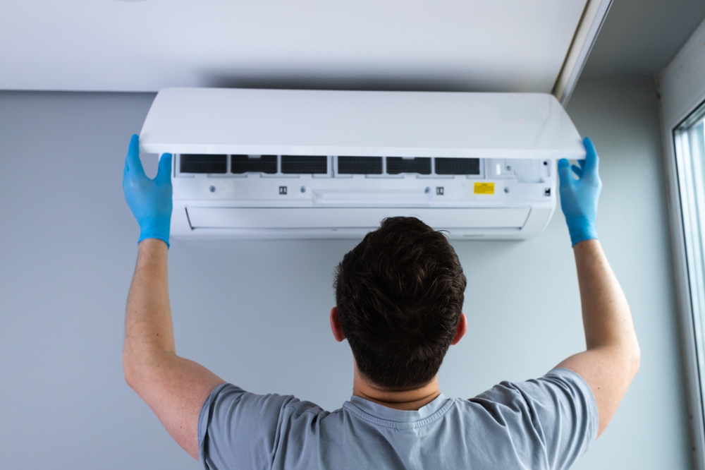 Technician Installing or Maintaining Air Conditioner Unit on Wall Amidst a Bright, Contemporary Room and Performing Professional HVAC Services with Care and Precision for Optimal Performance