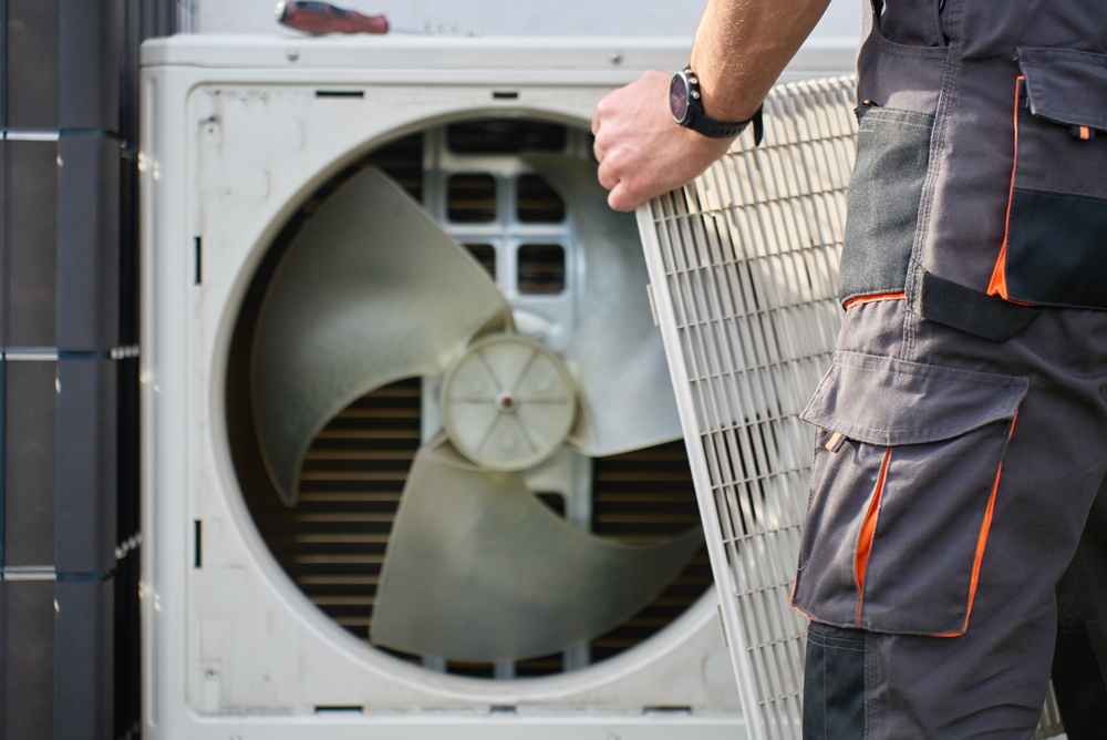 Technician removing front cover grille from outdoor heat pump unit during residential HVAC service. Concept of heat pump maintenance, repair and home heating and cooling 